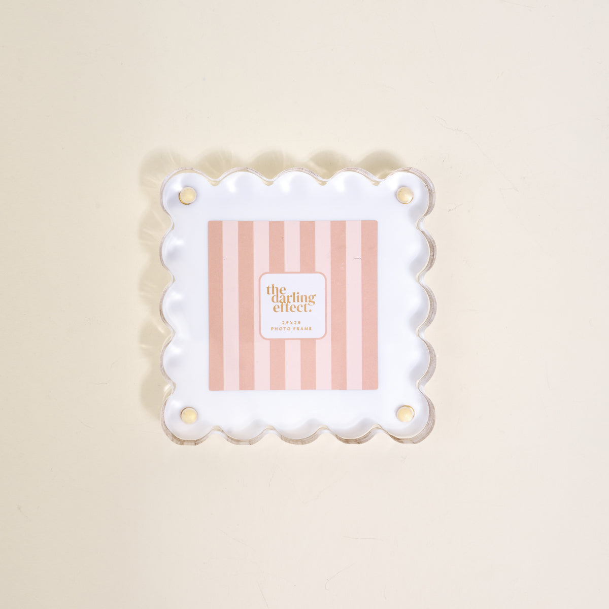 The Darling Effect's "White Little Moments Acrylic Picture Frame" showcases a square acrylic frame with scalloped edges and gold corner holes, displayed on a light beige surface.