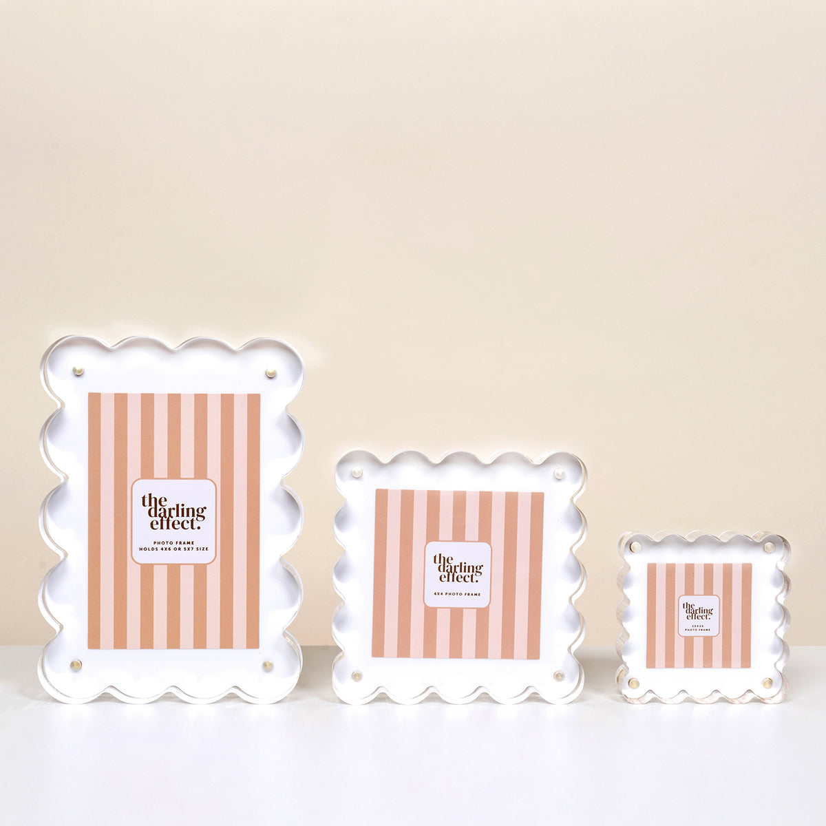 Three White Little Moments Acrylic Picture Frames by The Darling Effect, with scalloped edges, gold screws, and magnetic closures. Each frame has pink and white vertical stripes and a "gifting effect" label, displayed from largest to smallest.