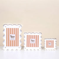 Three White Little Moments Acrylic Picture Frames by The Darling Effect, with scalloped edges, gold screws, and magnetic closures. Each frame has pink and white vertical stripes and a "gifting effect" label, displayed from largest to smallest.