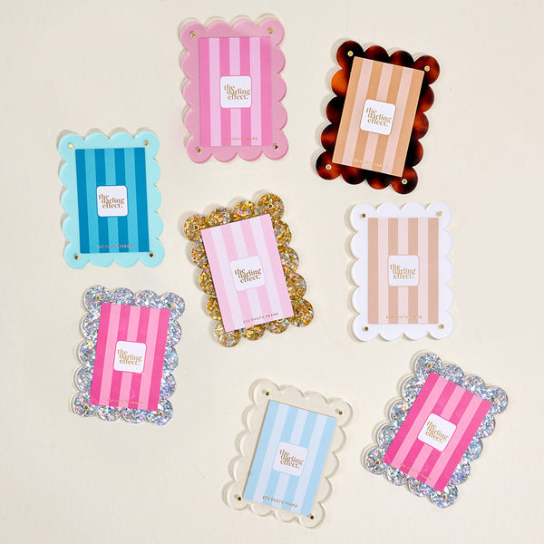 Eight scalloped, rectangular hair clips in assorted colors and patterns are arranged on a light surface, each next to a White Mini Acrylic Picture Frame Magnet from The Darling Effect that highlights their vibrant hues.