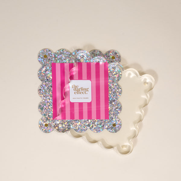 The Darling Effect Silver Glitter Square Scalloped Acrylic Picture Frame features modern design with a wavy clear border and silver glitter, shown displaying a pink and white striped card reading "the darling effect.