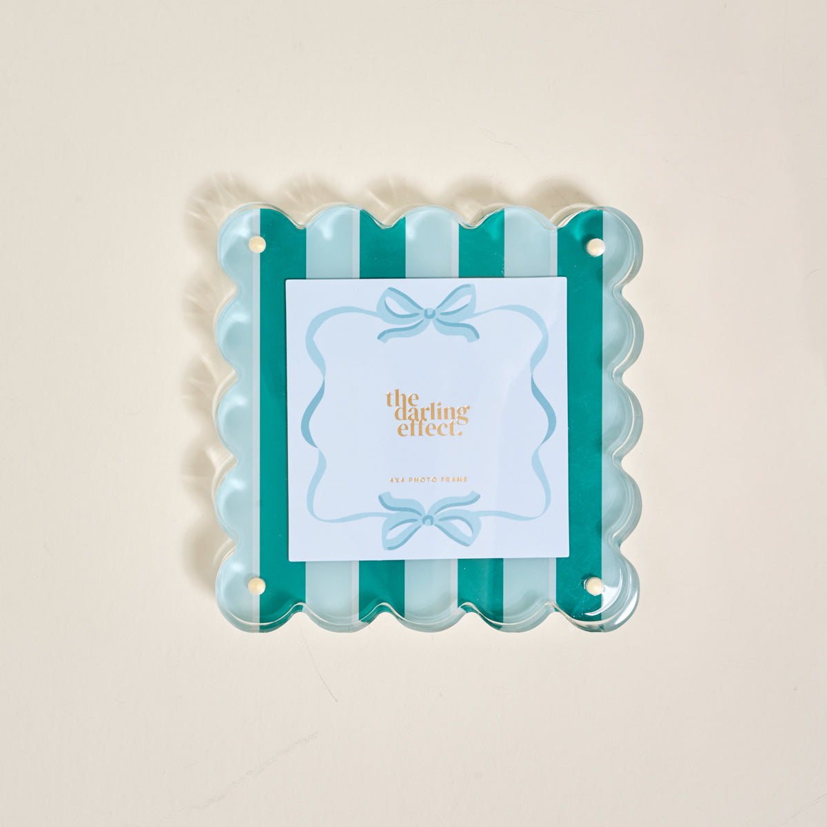 The Sicily Stripes Teal Square Scalloped Acrylic Picture Frame by The Darling Effect features teal and light blue striped scalloped edges and a magnetized design. The center card displays "the darling effect" in gold with blue bow illustrations.