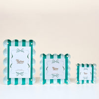 Three Sicily Stripes Teal Square Scalloped Acrylic Picture Frames by The Darling Effect, featuring teal and white stripes, bow accents, and a modern design, are arranged from largest to smallest on a white surface.