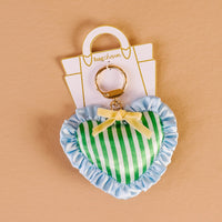 The Darling Effect's Cool Crush Puffy Heart Bag Charm features a heart shape with green and white stripes, blue ruffled trim, and a yellow bow on a gold keyring—an eye-catching accessory for your bag.