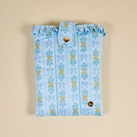 The Darling Effect’s Oh So Fancy Blue Book Cover features light blue puffy polyester with floral and bow accents, a gold snap closure, and a small round gold tag—perfect for cute book protection—shown on a beige background.