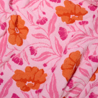 Close-up of The Darling Effect’s Poppin' Petals Hot Pink Cozy Dreams Luxe Blanket, a super-soft microfiber throw with orange flowers, small pink blooms, and leafy details. The ultra-plush blanket is pink and shown slightly crumpled.