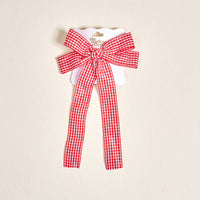 The Gingham Red Double Take Hair Bow by The Darling Effect features a red and white checkered fabric with two long tails, perfect for hair accessories, displayed on a white card against a light beige background.