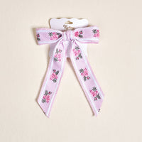 The Pink Heirloom Rosette Hair Bow by The Darling Effect features pink rose and green leaf embroidery on lavender, attached to a white branded card—an elegant addition to any hair accessories collection for stylish hair clip lovers.