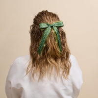 A woman’s wavy blonde hair is styled with The Darling Effect’s Everbloom Forest Green Lovely Layered Hair Bow—an elegant, floral-inspired accessory choice.