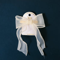 The Cream Sheer Pearl Hair Bow by the-darling-effect features an ivory sheer design with pearl trim, attached to a white card with the brand’s logo—a charming addition to your hair accessories.