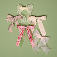The Cream Sheer Pearl Hair Bow by the-darling-effect is displayed on a green background, showcasing its elegant sheer fabric accented with pearls for a charming, decorative look.