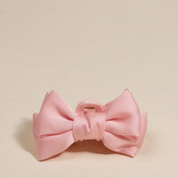 The Darling Effect's Blush Mini Satin Bow Claw Clip, featuring a pink satin bow and light pink plastic clasp, is displayed on a plain cream background.