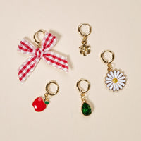 This set of four gold earrings features a red and white gingham bow, gold flower, white daisy with yellow center, and red apple—perfect for mixing and matching with The Darling Effect Apple of My Eye The Ultimate Charm Pack.