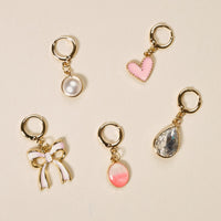 The Darling Effect’s Blush Crush The Ultimate Charm Pack features five gold keychain charms—a white pearl, pink heart, clear teardrop gem, pink and white bow, and a pink oval gem—perfect for scrunchie sets or statement necklaces.
