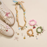 Add a playful touch with The Darling Effect's Fruit Frenzy The Ultimate Charm Pack: colorful scrunchies with cherry, bee, and shell charms—plus bow-adorned cream sneakers, floral scarf necklaces, and statement pieces.