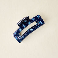 The Endless Daydream Navy Claw Clip by the-darling-effect features a dark blue base with small light blue and white floral prints, displayed on a light beige background.