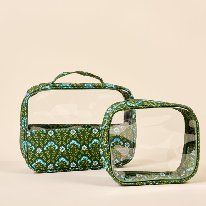 The Darling Effect’s Everbloom Forest Green Clearly Chic Cosmetic Bag Set features two rectangular clear bags with green and blue patterned edges and handles, displayed upright and angled on a plain beige background.