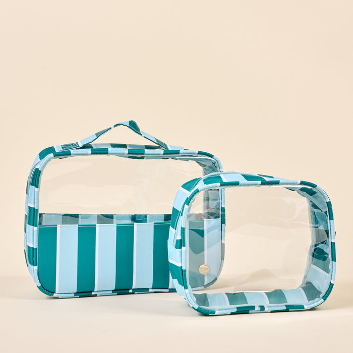 The Darling Effect’s Sicily Stripes Teal Clearly Chic Cosmetic Bag Set features two clear bags with teal and white striped edges—one upright with a top handle, the other smaller and angled in front.