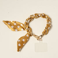 The Darling Effect’s Honey Blossom Call Me Later Phone Scarf pairs a daisy-print satin ribbon and gold braid with a clear badge holder for a stylish, practical accessory.
