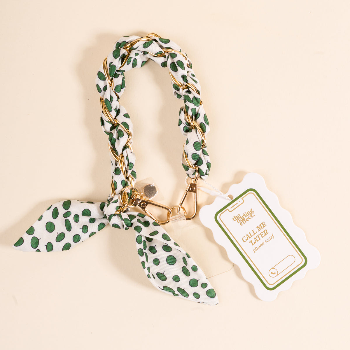 The Darling Effect Olive Dot Call Me Later Phone Scarf features green polka dots, a gold-tone chain, bow, and scalloped tag reading THE SNAZZY PAWS CLUB - CALL ME with room for your phone—an adorable accessory for your pup!.