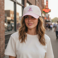 A woman wears a cream t-shirt and The Darling Effect Cowgirl Boots Classic Canvas Hat, featuring a relaxed fit, tan canvas, pink brim, and pink cowboy boots patch—perfect for everyday wear.