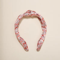The Everbloom Dusty Rose Classic Twist Headband by The Darling Effect features a top knot and floral pattern in red, pink, and gray. This versatile accessory is shown on a plain light background.