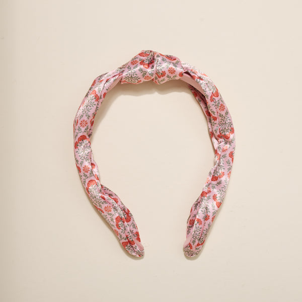The Everbloom Dusty Rose Classic Twist Headband by The Darling Effect features a top knot and floral pattern in red, pink, and gray. This versatile accessory is shown on a plain light background.