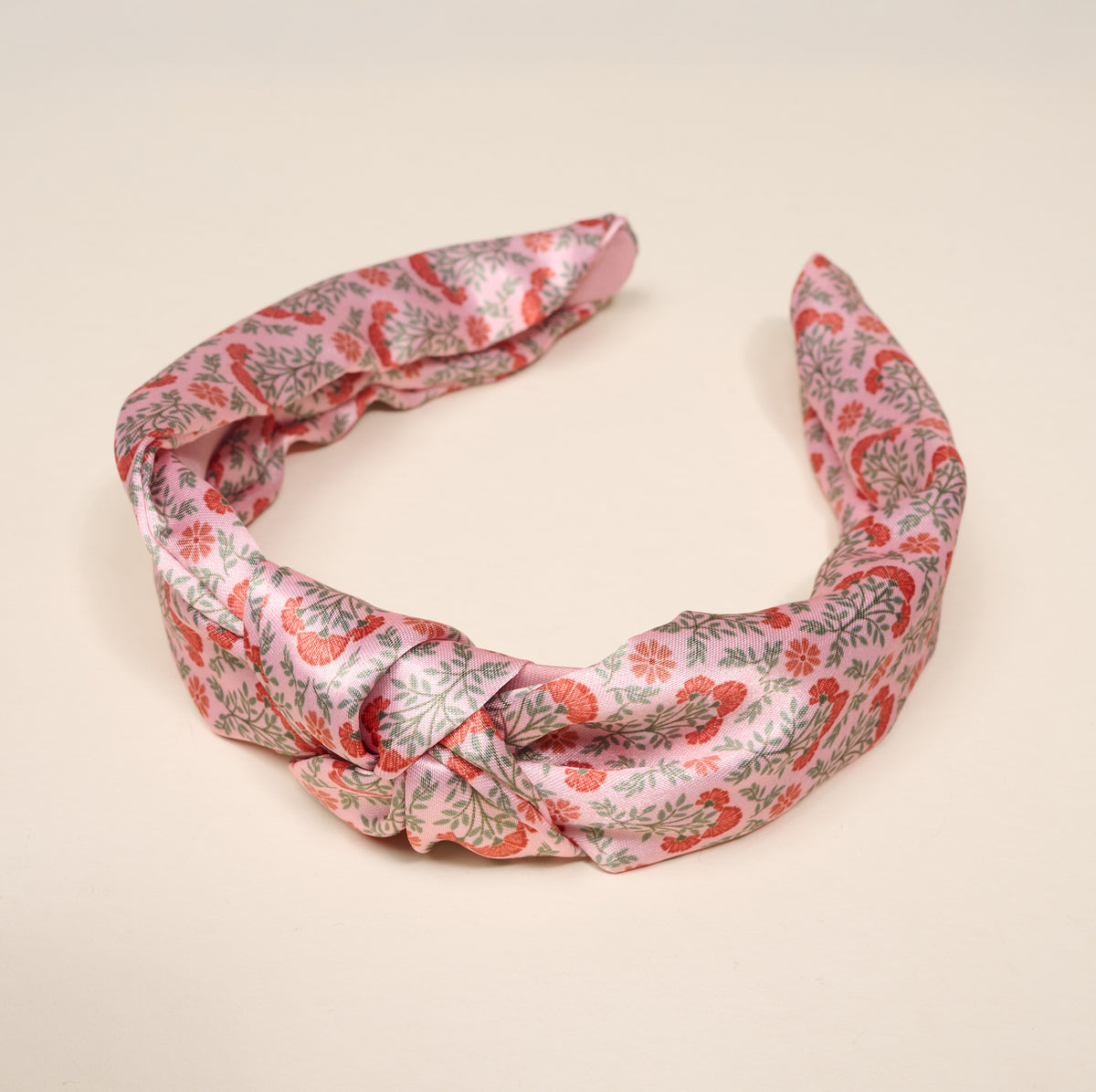 The Darling Effect Everbloom Dusty Rose Classic Twist Headband features a pink satin design with a twist knot detail and a red and green floral pattern, making it a versatile hair accessory.