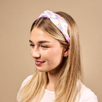 A young woman with long blonde hair smiles softly in a white shirt and The Darling Effect's School's In Session Classic Twist Headband—a versatile pastel accessory against a beige background, perfect for any look.