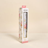 A chic workspace accessory, the Endless Daydream Cream Style Station Desk Mat by The Darling Effect comes in a white rectangular box with pink, yellow, and green floral designs and a window showing the non-slip desk mat inside.