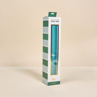 The Sicily Stripes Teal Style Station Desk Mat by The Darling Effect comes in upright white packaging with green stripes and a window displaying the blue mat inside. Labeled "desk mat" at the top, it's perfect for workspace transformation.
