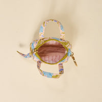 The Darling Effect’s Poppin' Petals Aqua Itty Bitty Duffle Bag Charm is a small fabric handbag with pastel florals, gold clasp, and two handles. An open zipper reveals its pink lining for a pop of color and style.