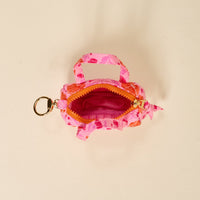 The Poppin' Petals Hot Pink Itty Bitty Duffle Bag Charm by The Darling Effect features pink and orange patterns, a partially open zipper showing its pink interior, two handles, and a gold keyring, photographed from above on a light background.
