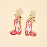 Cowgirl Boot Beaded Earrings by The Darling Effect feature vibrant pink boots with white pearls and green and pink floral beadwork, displayed on a light beige background.
