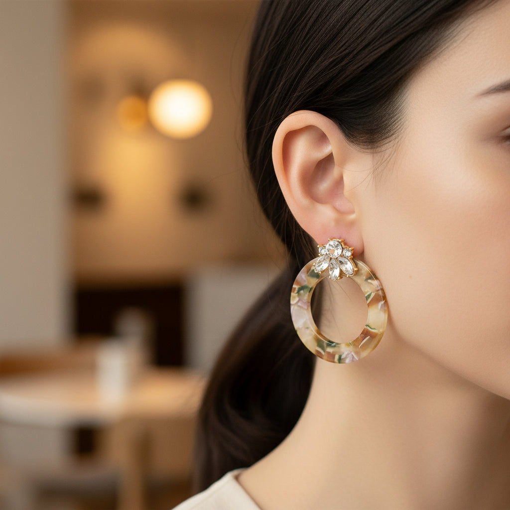 A close-up of a woman's ear wearing The Darling Effect Amber Drift Glow Getter Earrings—lightweight, marbled acetate hoops accented with sparkling, clear stones.