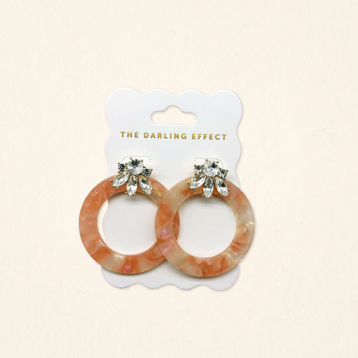 The Darling Effect Rose Quartz Glow Getter Earrings are lightweight, round, peach-marbled statement earrings with crystal-embellished posts, displayed on a branded white card.