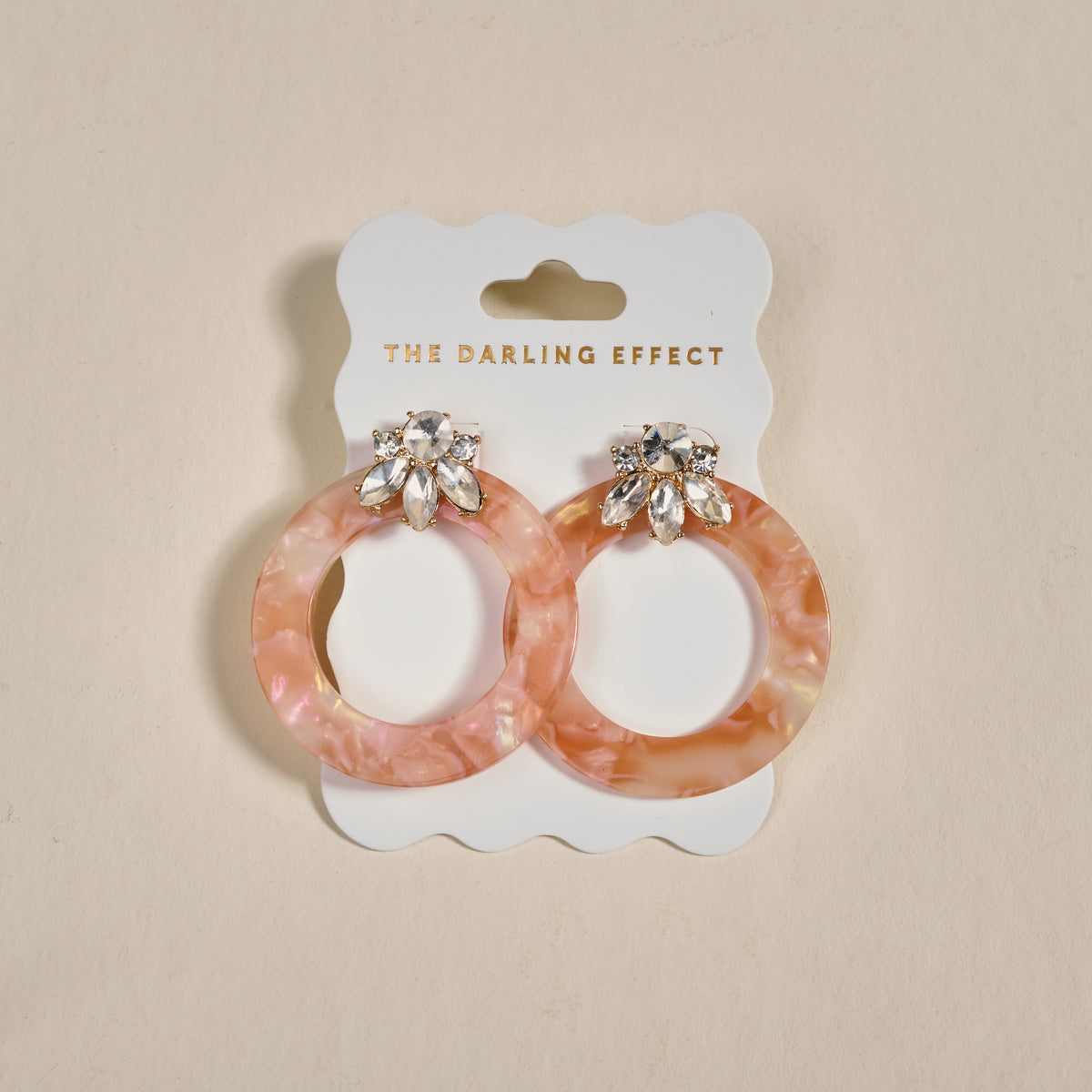 The Darling Effect’s Rose Quartz Glow Getter Earrings—pink marbled statement earrings with jeweled studs—are displayed on a white card with the brand name, set against a neutral background.