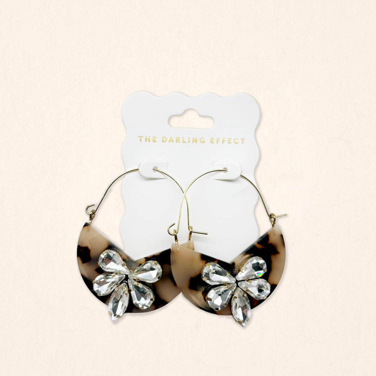 Blonde Tortoise Marble Bloom Hoop Earrings by The Darling Effect feature gold hoops with marbled semicircle tortoiseshell pendants, each embellished with clear rhinestone butterfly designs and displayed on a branded white card.
