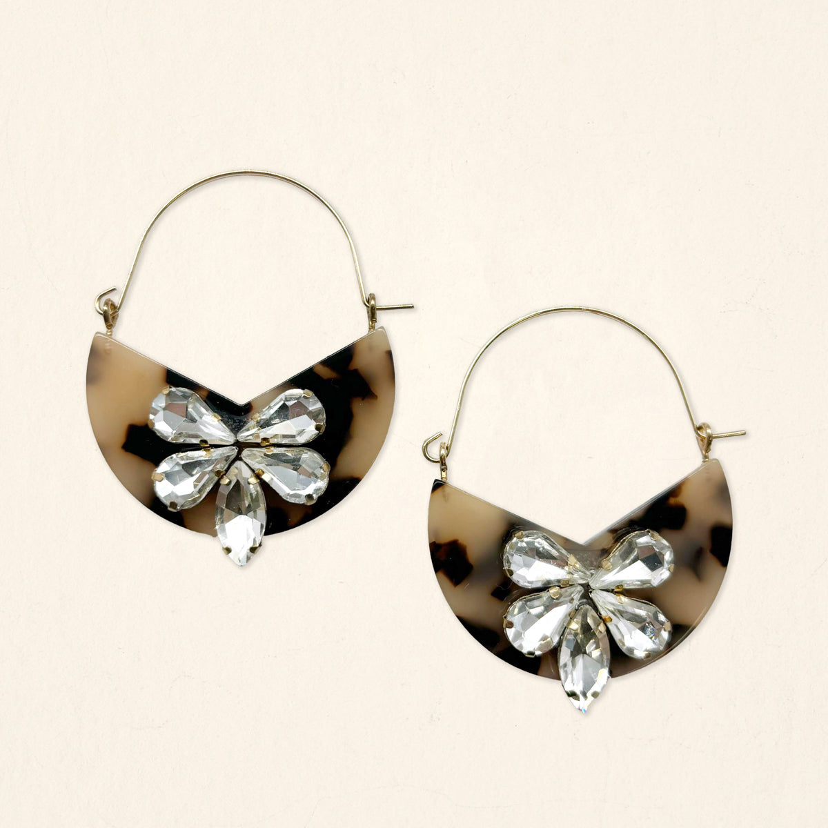 The Darling Effect’s Blonde Tortoise Marble Bloom Hoop Earrings are large, lightweight hoops featuring half-moon tortoiseshell pendants and clusters of clear, teardrop crystals in a floral design.