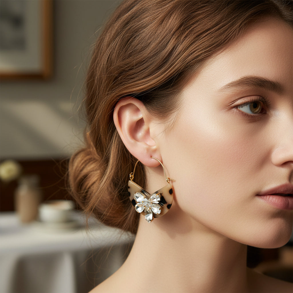 A woman with light skin and brown hair in a low bun wears The Darling Effect's Blonde Tortoise Marble Bloom Hoop Earrings. Lightweight and bold, the statement hoops stand out against a softly blurred indoor background.