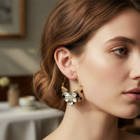 A woman with light skin and brown hair in a low bun wears The Darling Effect's Blonde Tortoise Marble Bloom Hoop Earrings. Lightweight and bold, the statement hoops stand out against a softly blurred indoor background.
