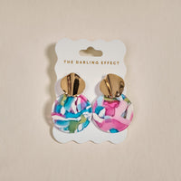 The Darling Effect Aurora Marble Muse Earrings feature gold-tone tops and large, round drops with a colorful marbled pattern in pink, blue, white, and green, displayed on a branded card.