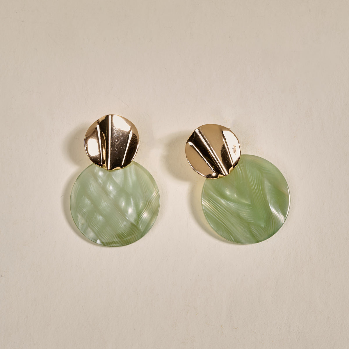 The Darling Effect's Sage Serenity Marble Muse Earrings feature lightweight, shiny gold studs and large, round marbled light green dangles, beautifully displayed on a light beige background.