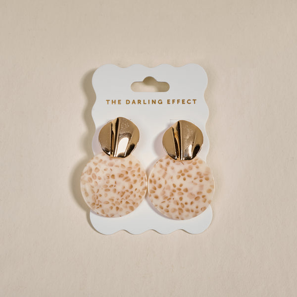 The Darling Effect's Toffee Glow Marble Muse Earrings feature gold metallic tops and round, cream-toned textured dangles, shown on a branded card against a neutral background.
