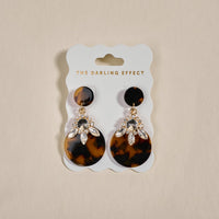 The Darling Effect's Totally Tortoise Show Stopper Earrings feature lightweight tortoiseshell-patterned discs with sparkling rhinestones, displayed on a branded card.