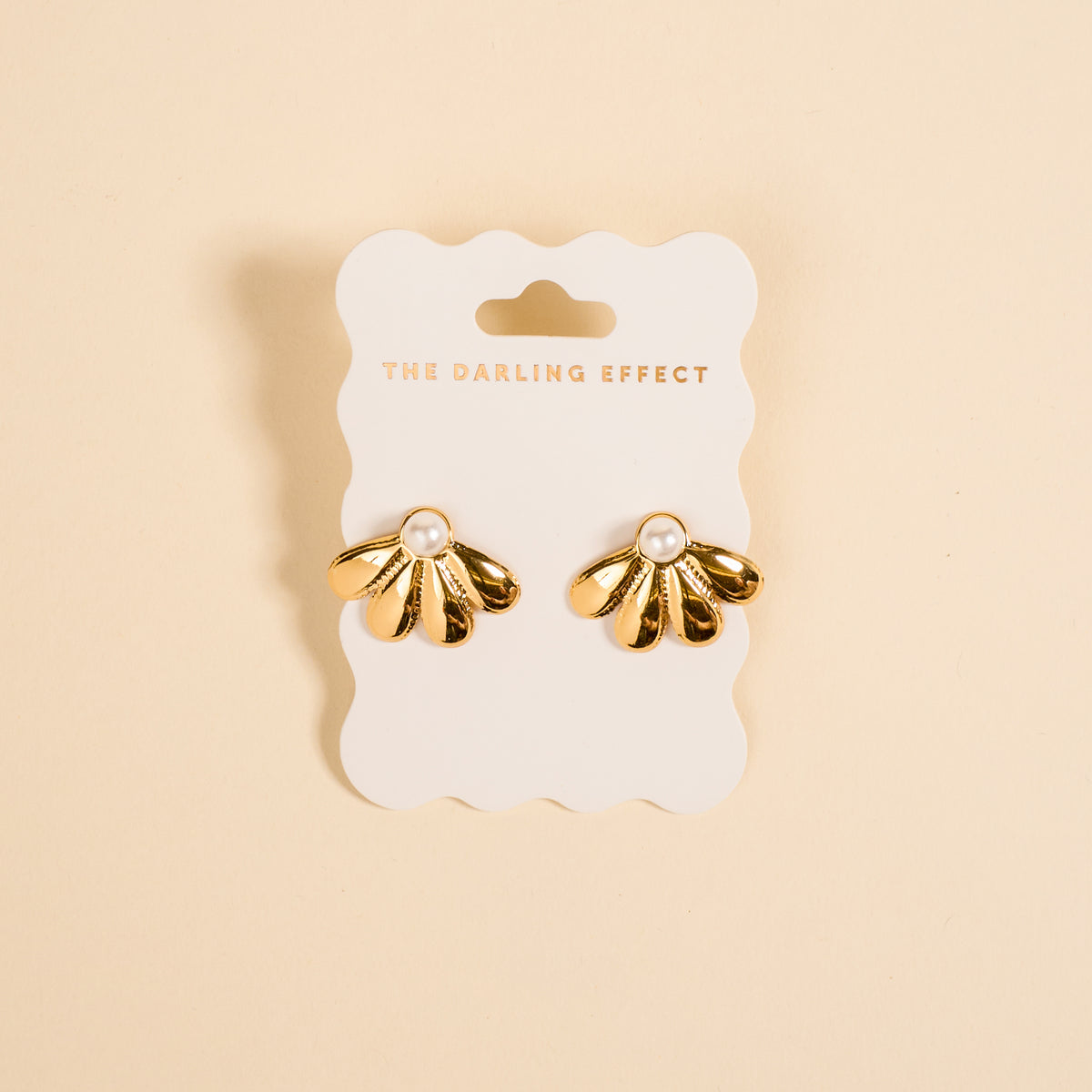 The Daisy Doo Standout Earrings by The Darling Effect are golden, high-shine floral earrings with pearl centers, displayed on a branded white card against a beige background. Ideal for special occasions.