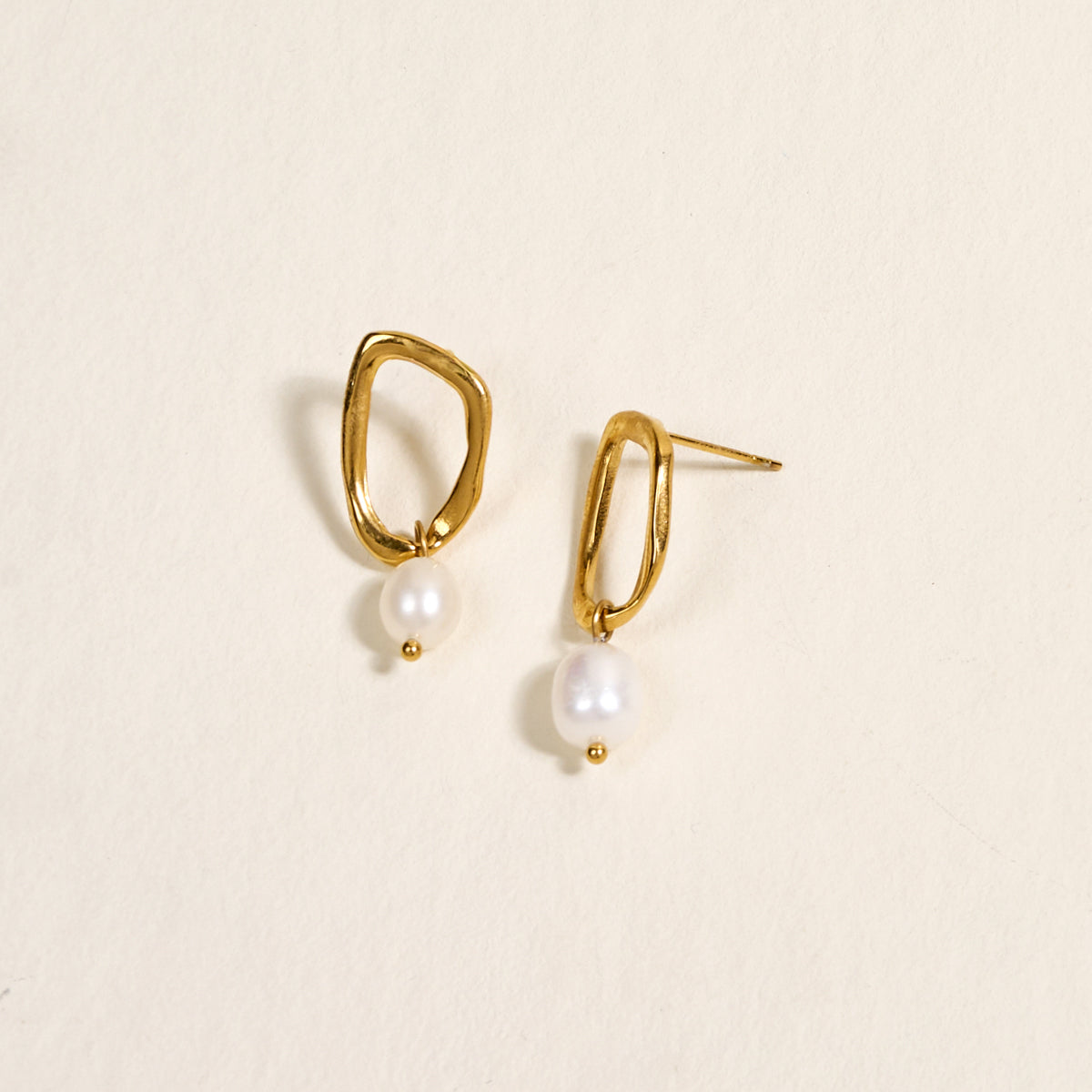 The Darling Effect's Dainty Drift Standout Earrings, featuring irregular shapes and white pearls, shine against a cream background—perfect for special occasions.