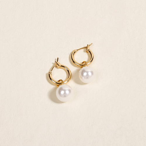 The Darling Effect’s Dainty Pearl Standout Earrings feature a high-shine golden hoop with a single round white pearl, shown against a light beige background.