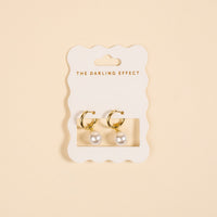 The Darling Effect’s Dainty Pearl Standout Earrings feature golden hoops with pearl drops, elegantly displayed on a scalloped white card—perfect for making a statement.