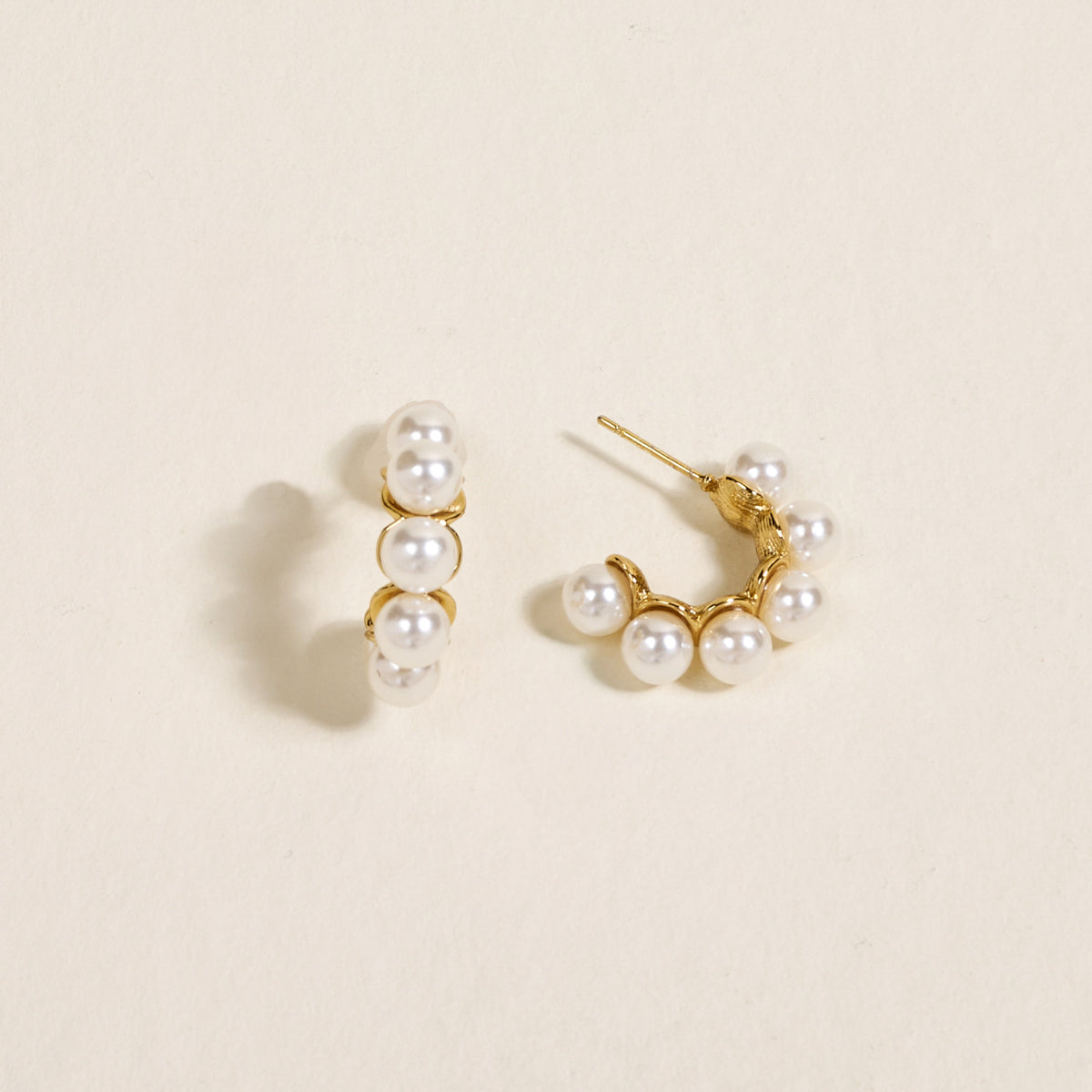The Darling Effect’s Power Pearl Standout Earrings feature a high-shine gold finish and four evenly spaced white pearls, showcased on a light cream background—an elegant jewelry statement.